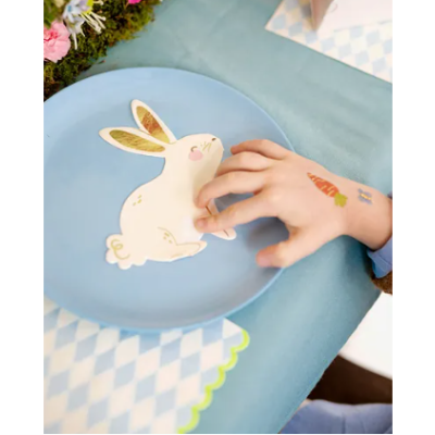 Prato azul com desenho de coelho branco sendo tocado por mão de criança com tatuagens temporárias.