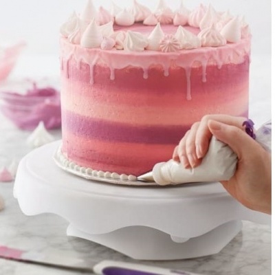 Bolo rosa e roxo com glacê a ser decorado numa base branca giratória