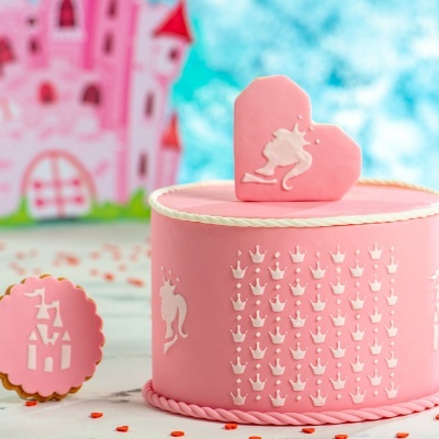 Bolo cor-de-rosa decorado com coroas e silhuetas de princesa e biscoitos decorados