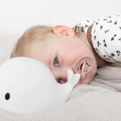 Bebé de pijama com chucha ao lado de candeeiro baleia branco