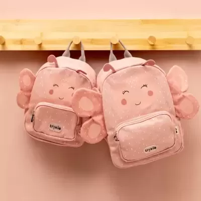 Duas mochilas cor-de-rosa para crianças com asas e detalhes felpudos penduradas num cabide de madeira