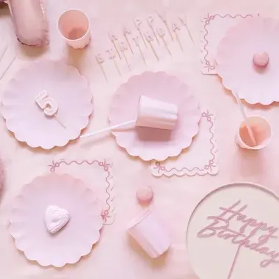 Conjunto de festa de aniversário rosa claro com pratos, copos, velas e balões em números.