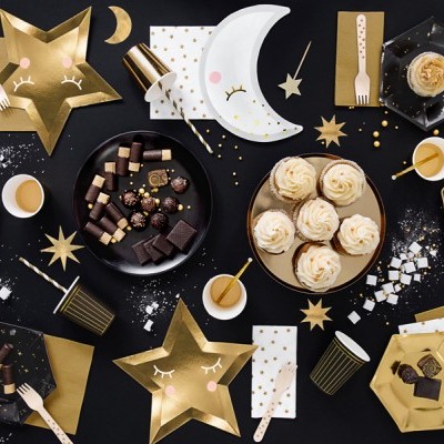 Mesa de festa com decoração em dourado, branco e preto, pratos descartáveis em formas de estrela, lua e hexágono e doces