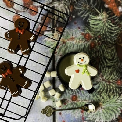 Biscoitos de gengibre em forma de bonecos, caneca preta com bebida quente e malvaviscos, superfície festiva com pinheiros e bagas vermelhas