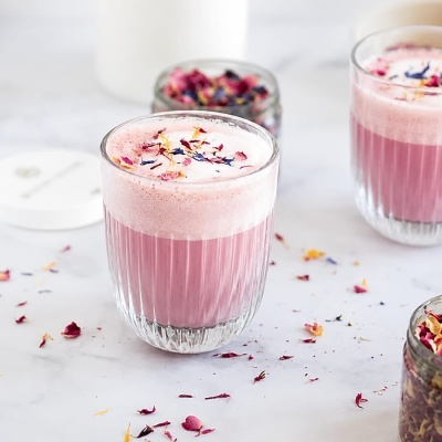 Dois copos de vidro com bebida rosa e espuma decorada com pétalas