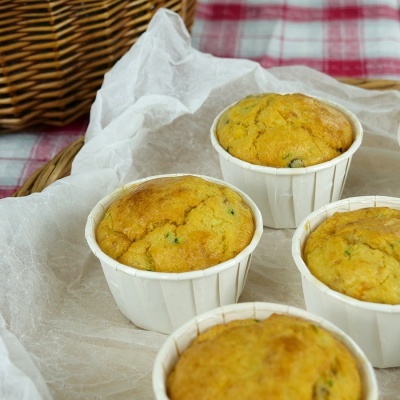 Quatro muffins amarelos em copos de papel branco sobre papel manteiga, com cesta de vime e toalha xadrez ao fundo