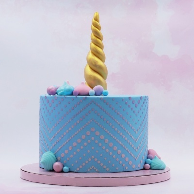 Bolo decorado azul com padrões cor-de-rosa e corno dourado no topo