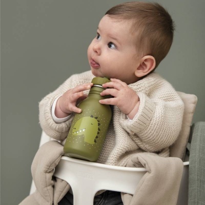 Copo infantil verde com desenho de dinossauro segurado por criança em cadeira branca