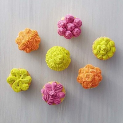 Sete cupcakes decorados coloridos em padrão floral e espiral sobre fundo cinza claro