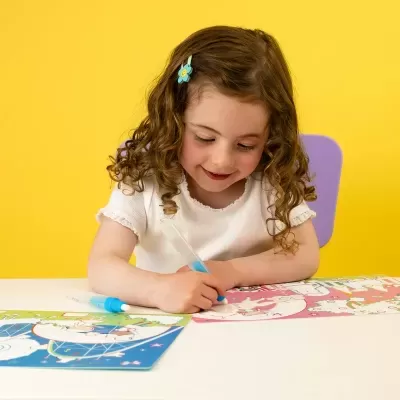 Criança desenhando com caneta líquida azul em folha colorida com desenhos de unicórnios