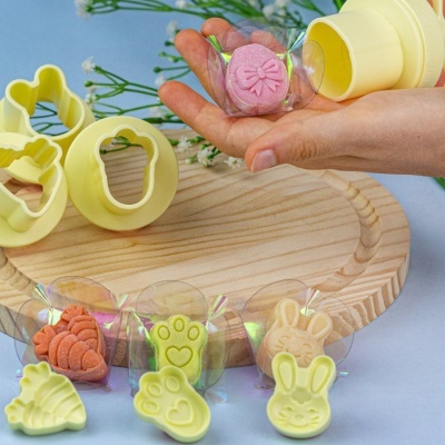 Conjunto de cortantes amarelos em forma de coelho, pata, peixe e folha com biscoitos decorados e embalados sobre tábua de madeira.