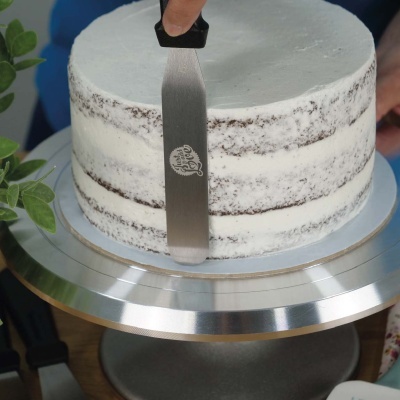 Bolo redondo com cobertura branca em suporte metálico com espátula