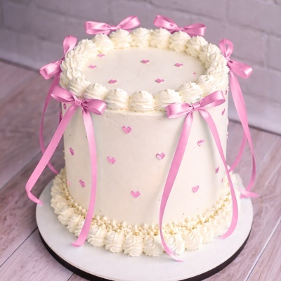 Bolo branco decorado com laços rosa e pequenos corações cor-de-rosa
