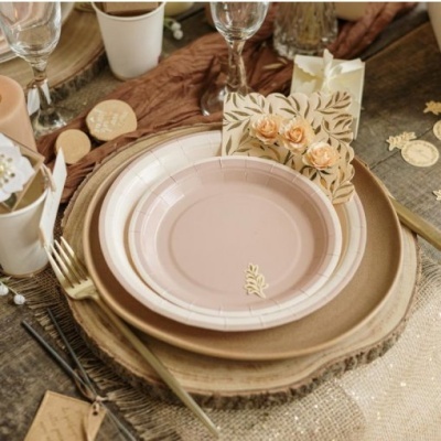 Mesa posta com prato rosa claro, prato rústico de madeira, talheres dourados e cartão decorativo com flores e folhas