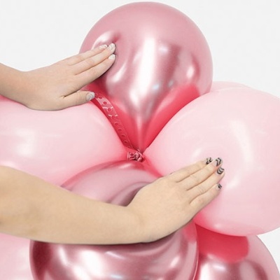 Balões rosa e rosa metálico agrupados com mãos femininas pressionando