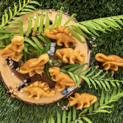 Figuras de dinossauros castanhos aveludados sobre disco de madeira com folhas verdes e pedras sobre relva sintética