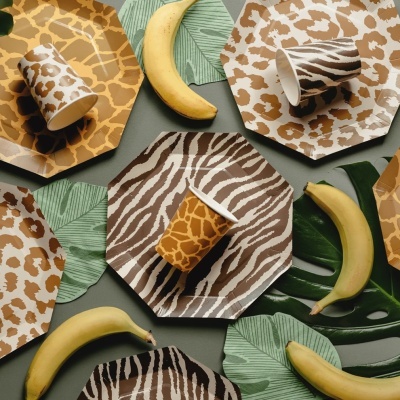Pratos e copos descartáveis com padrões de pele de animal e folhas verdes com bananas amarelas.
