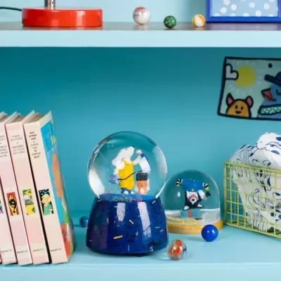 Globo de neve decorativo azul, livros coloridos, bolas de vidro e cesta amarela com tecido