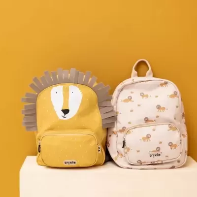 Duas mochilas infantis com design de leão em amarelo e creme sobre fundo amarelo.