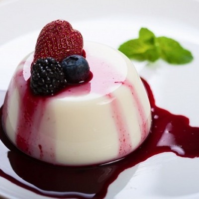 Panna cotta branca com molho vermelho e frutas vermelhas num prato branco.