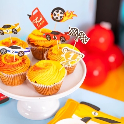 Cupcakes amarelo e laranja com decoração de corrida e carros sobre placa branca.