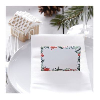 Cartão de lugar floral de Natal sobre guardanapo branco e prato com decoração natalícia ao fundo.