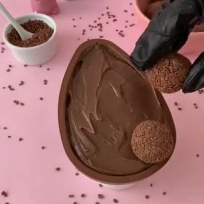 Preparo de ovo de Páscoa de chocolate recheado e decorado com brigadeiros e granulado.