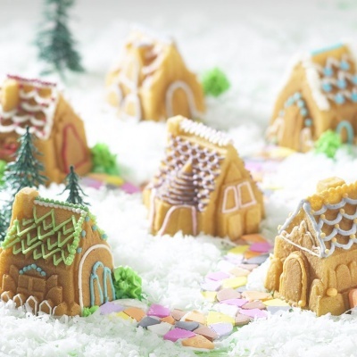Casas de biscoito gengibre decoradas com glacê colorido e pequenas árvores sobre neve artificial com caminho de doces