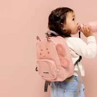 Mochila infantil rosa com padrão branco e borboleta, etiqueta trixie, usada por criança com garrafa rosa