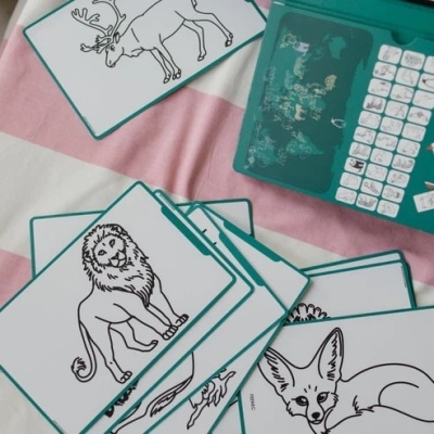 Cartas infantis com desenhos de animais em preto e branco junto a um dispositivo verde com teclado