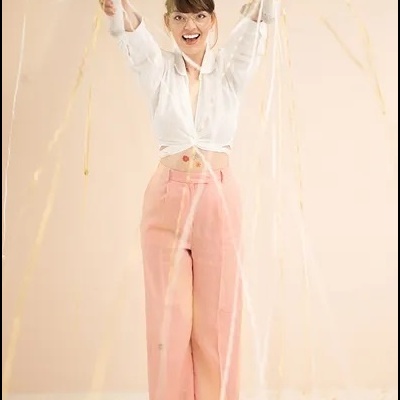 Mulher sorridente com camisa branca e calças rosa entre confete dourado