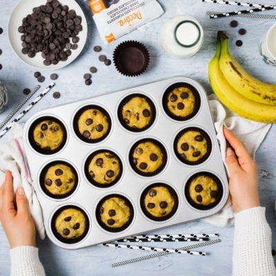 Tabuleiro com 12 muffins de chocolate, bananas, leite e gotas de chocolate num fundo cinza