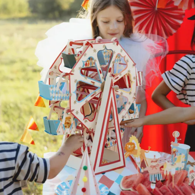 Brinquedo roda-gigante em madeira com crianças vestidas a rigor num piquenique ao ar livre