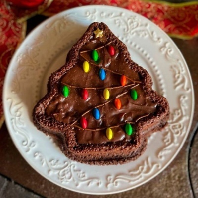 Bolo de chocolate em forma de árvore de Natal com confeitos coloridos num prato branco