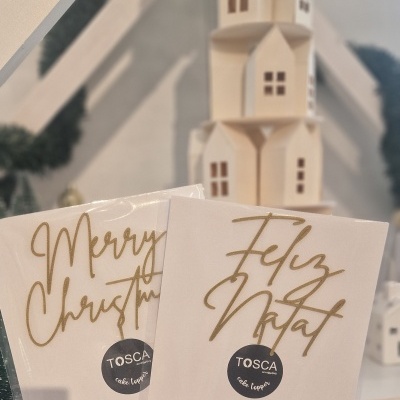 Caixas ou cartões de Natal brancos com texto dourado e autocolante TOSCA, ao fundo decoração branca e guirlanda