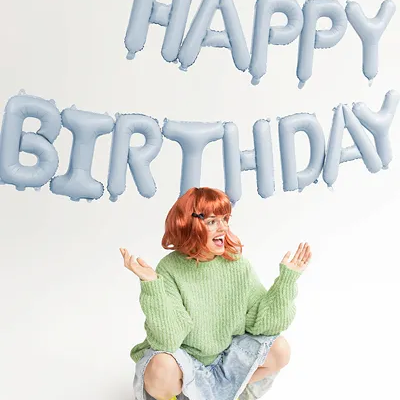 Balões azuis HAPPY BIRTHDAY em fundo branco com mulher agachada a sorrir