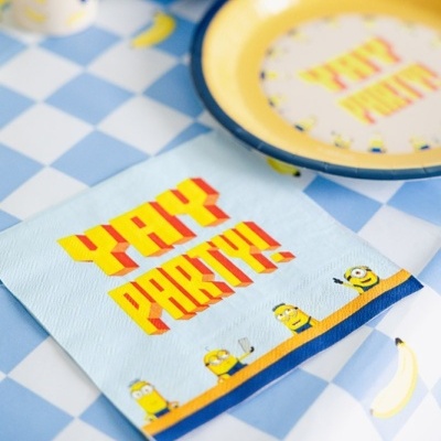 Guardanapo azul com texto YAY PARTY e personagens Minions ao lado de prato amarelo com texto similar sobre mesa xadrez azul e branca