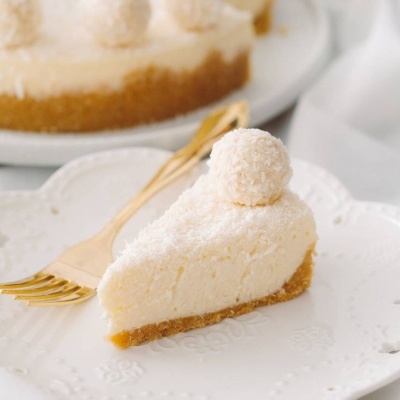 Fatia de tarte branca com base castanha e esfera de coco numa prato branco com garfo.