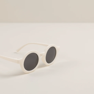 Óculos de sol brancos com lentes redondas pretas sobre superfície branca.