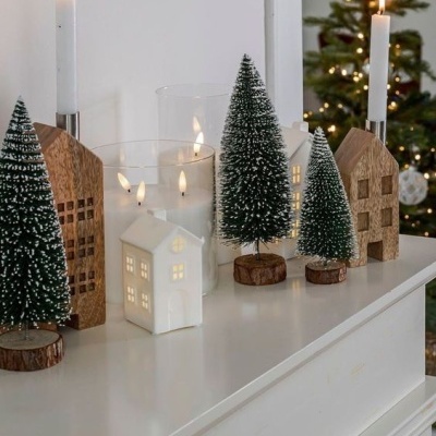 Decoração de Natal com casas iluminadas, árvores de pinheiro e velas sobre superfície branca