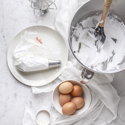 Utensílios de confeitaria com mistura branca, saco de pasteleiro, ovos e sal num fundo de mármore