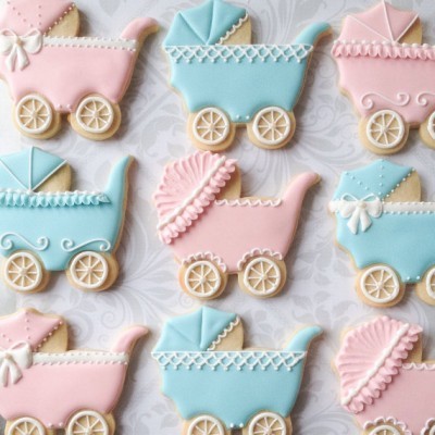 Biscoitos decorados em forma de carrinhos de bebé rosa e azul com glacê branco, sobre fundo branco com padrão