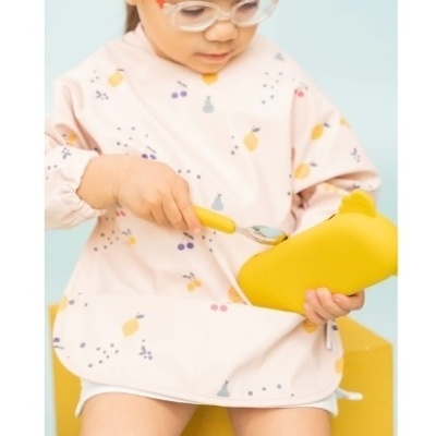 Criança com babete azul e colher com pote amarelo sentado em banco amarelo