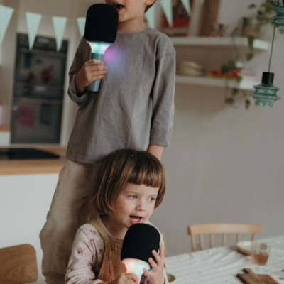 Duas crianças segurando microfones luminosos numa cozinha com tigela de pipocas à frente