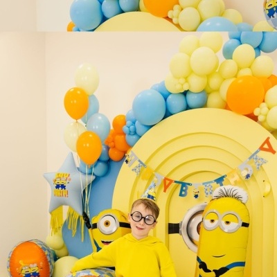 Criança com suéter amarelo e balões coloridos com decoração dos Minions em festa de aniversário