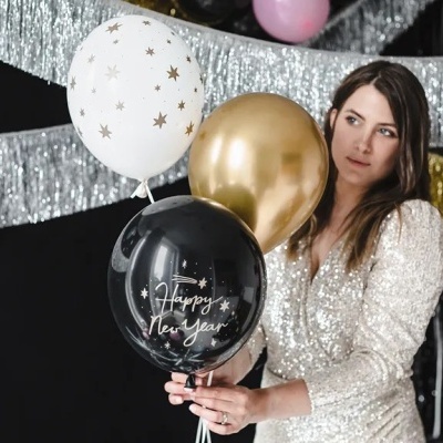 Mulher com vestido cintilante segura balões decorativos de Ano Novo em fundo festivo prateado e dourado