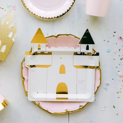 Prato em formato de castelo branco, dourado e preto sobre prato rosa com borda dourada