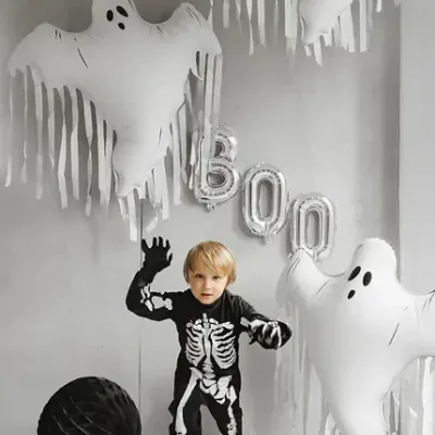 Criança em fato de esqueleto com balões de fantasmas e letras BOO para Halloween