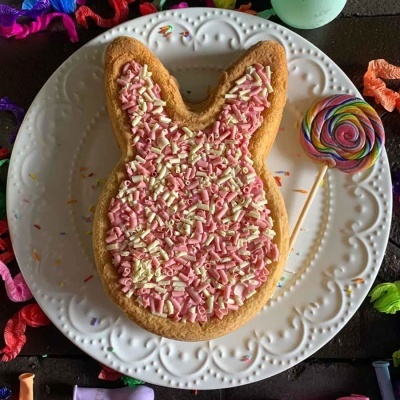 Biscoito em forma de cabeça de coelho com glacê e granulado rosa e branco num prato branco e pirulito colorido ao lado