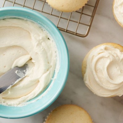 Tigela azul com creme de cobertura branca e faca, bolachas cobertas de creme branco ao redor